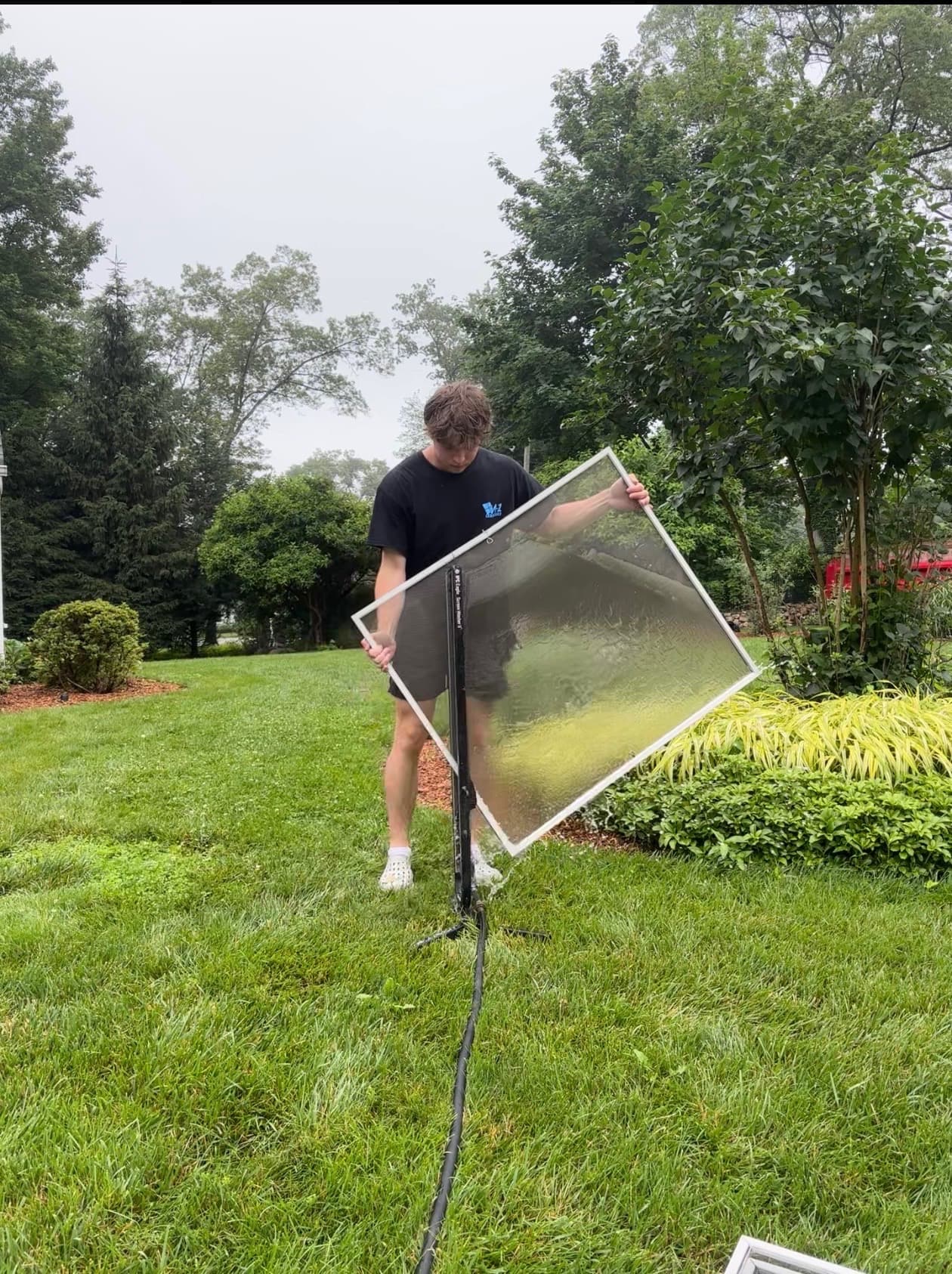 Anthony cleaning a window screen on a stand in the yard, A-1 Exterior shirt on