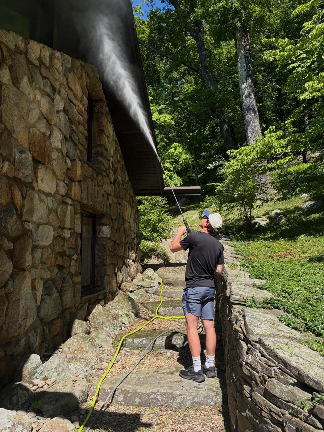 Anthony power washing the stone wall of a house