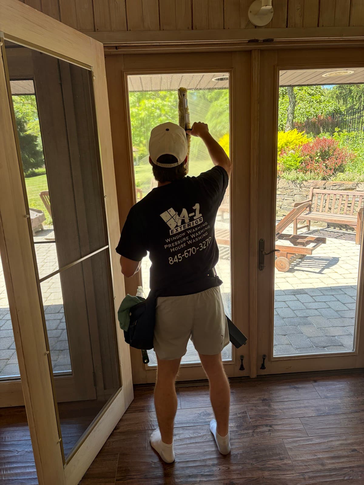 Anthony hand-squeegeeing a tall glass door in his A-1 Exterior shirt